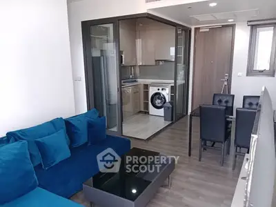 Modern living room with blue sofa and open kitchen featuring washing machine.