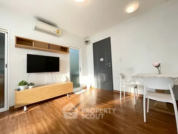 Bright modern living room with wooden flooring, wall-mounted TV, and dining area.