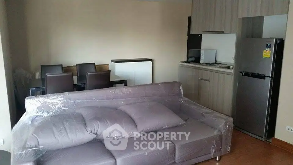 Modern living room with sleek kitchen and dining area, featuring a stylish sofa and contemporary appliances.