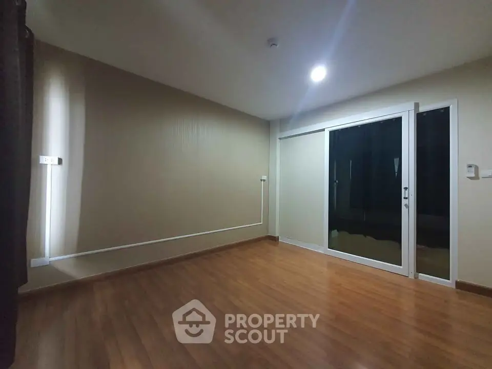 Spacious empty room with wooden flooring and large sliding glass door.