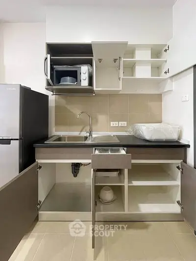 Modern kitchen with open cabinets, stainless steel sink, and microwave in a compact layout.