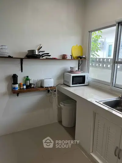 Cozy kitchen with open shelves, microwave, and window view in modern home.