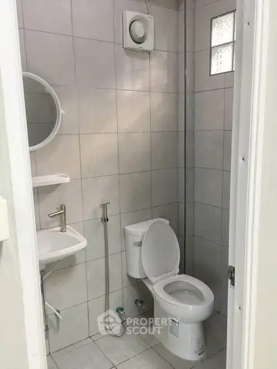 Compact bathroom with modern fixtures and tiled walls, featuring a round mirror and a small sink.