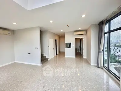 Spacious modern living room with large windows and city view, featuring sleek tile flooring and neutral decor.