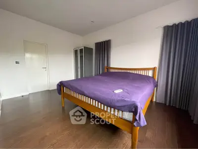 Spacious bedroom with wooden bed and purple bedding, featuring dark curtains and a sleek wardrobe.