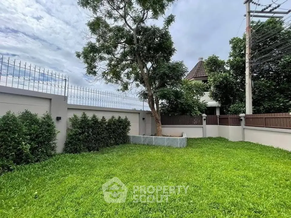 Spacious green garden with tree in a fenced residential area, perfect for outdoor activities.