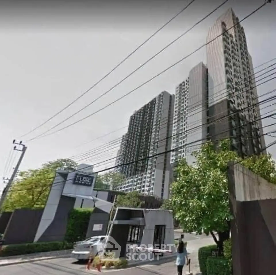 Modern high-rise condominium building with lush greenery and secure entrance.