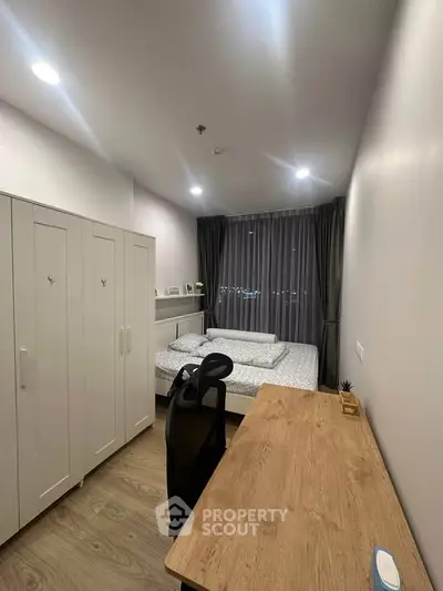 Modern bedroom with wooden desk and large wardrobe, featuring cozy lighting and city view.