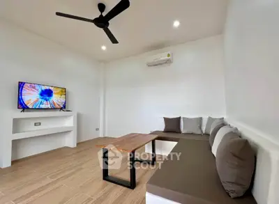 Modern living room with minimalist design, featuring a ceiling fan, wall-mounted TV, and cozy seating area.