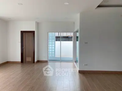Spacious unfurnished room with wooden flooring and sliding glass doors leading to a small balcony.
