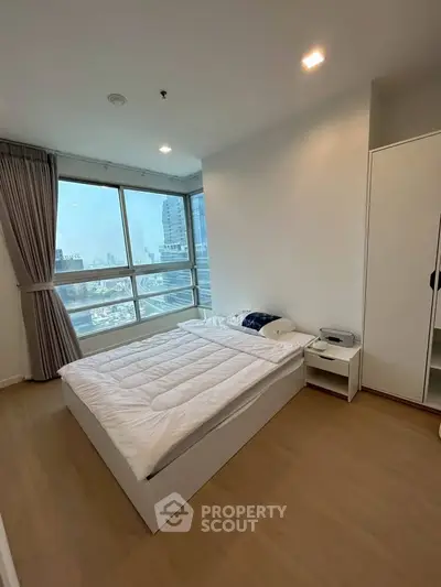 Modern bedroom with large windows offering stunning city views, featuring a cozy bed and sleek wardrobe.