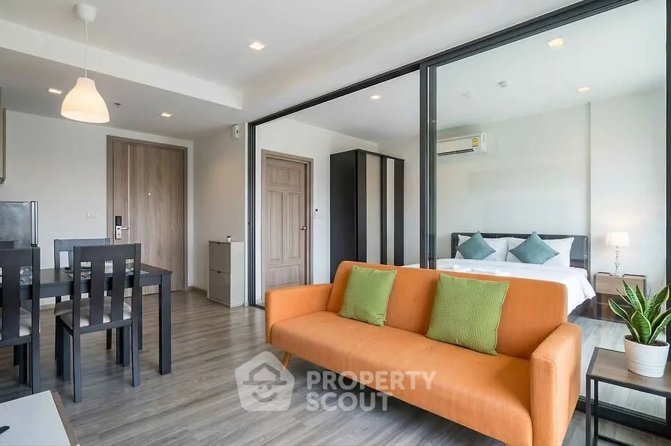 Modern open-plan living room with vibrant orange sofa and stylish dining area, leading to a cozy bedroom.
