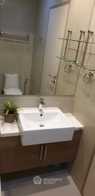 Modern bathroom with sleek sink, glass shelves, and elegant fixtures in a contemporary apartment.