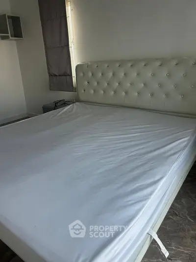 Spacious bedroom with elegant white tufted headboard and large window for natural light.