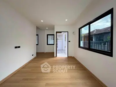 Spacious modern room with wooden flooring and large windows, ideal for versatile living space.