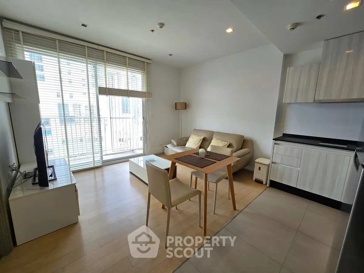 Modern living room with open kitchen and balcony view, featuring sleek furniture and natural light.