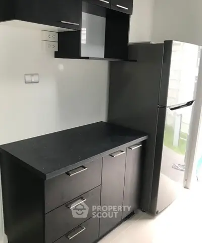 Modern kitchen with sleek black cabinetry and stainless steel fridge in a compact layout.