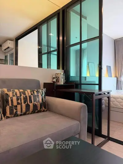 Modern living room with stylish decor and glass partition leading to bedroom
