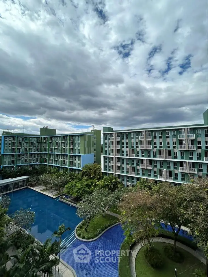 Stunning view of modern apartment complex with pool and lush greenery under dramatic skies.