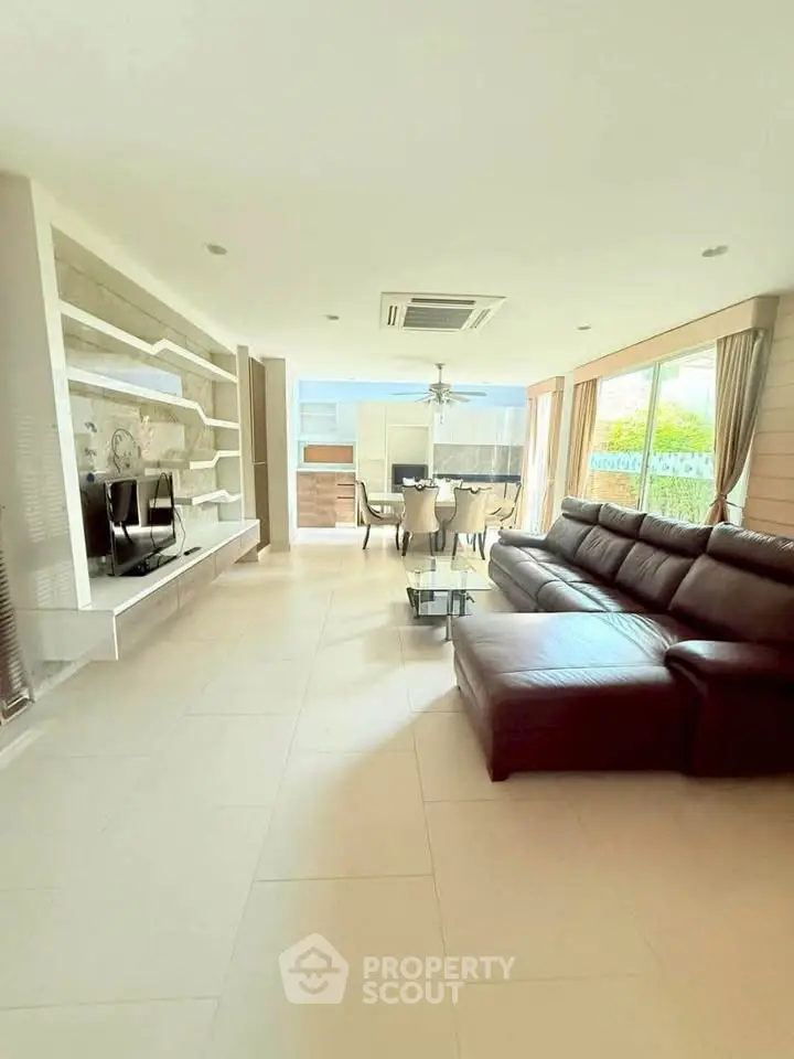 Spacious modern living room with leather sofa and dining area, featuring large windows and elegant decor.