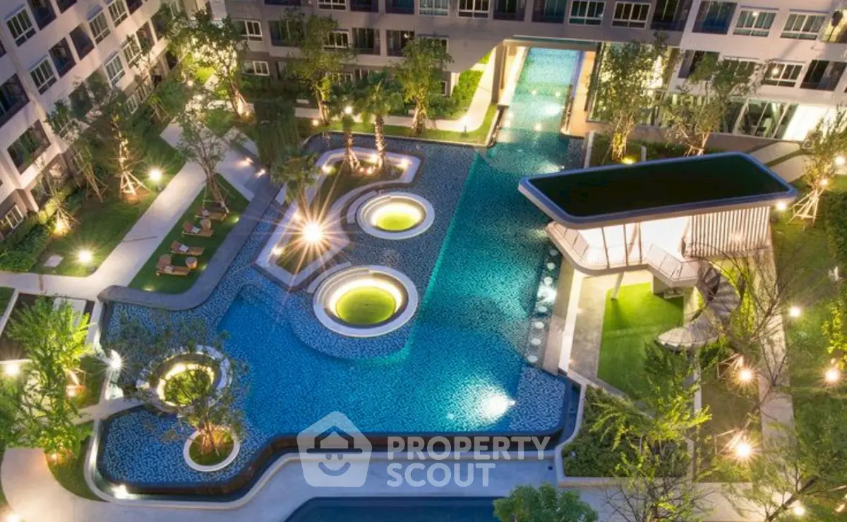 Luxurious apartment complex with stunning illuminated pool and lush greenery at night.