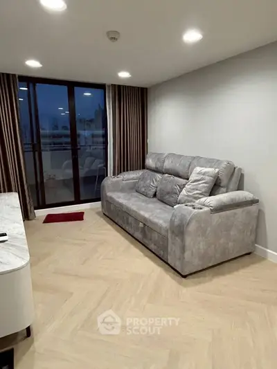 Modern living room with stylish gray sofa and elegant parquet flooring, featuring large windows for natural light.