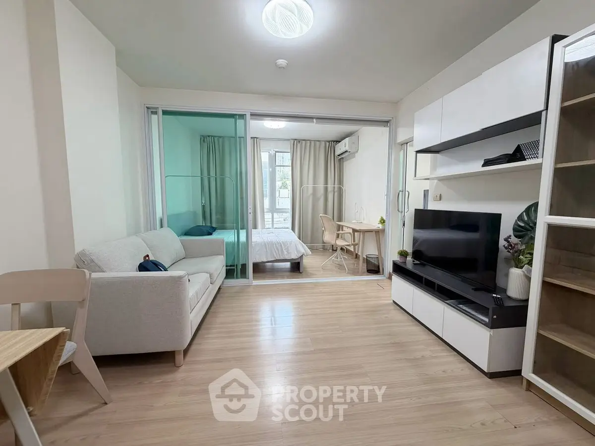 Modern open-plan living room with sliding glass doors to bedroom, featuring sleek furniture and natural light.