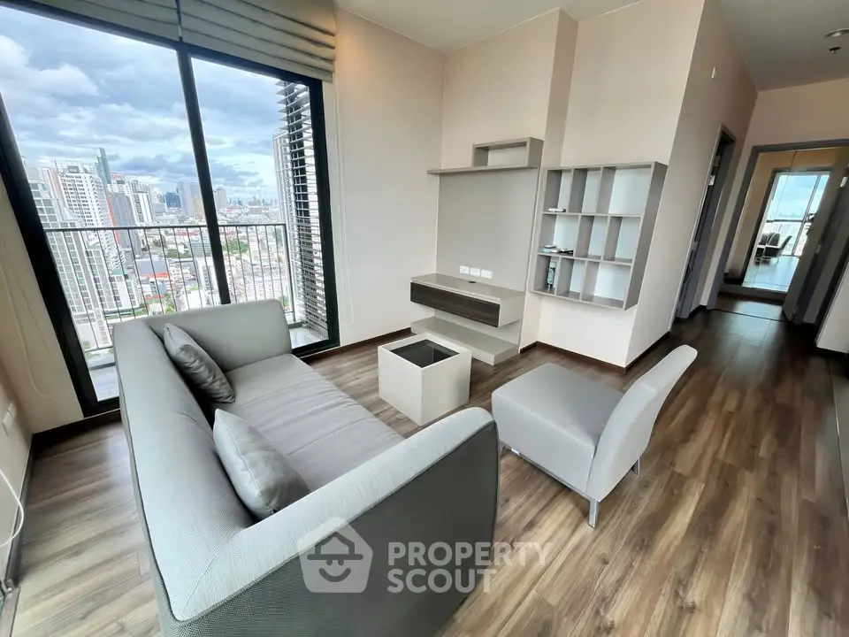 Modern living room with city view, featuring sleek furniture and floor-to-ceiling windows.