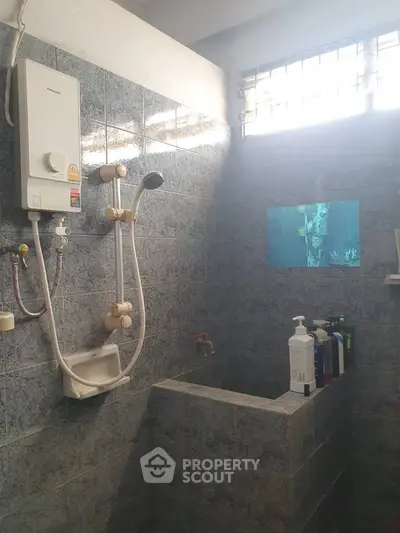 Compact bathroom with shower and water heater, featuring tiled walls and natural light from a window.
