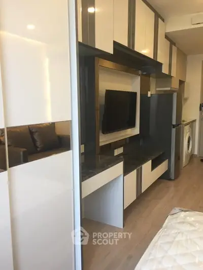 Modern apartment interior with sleek cabinetry and built-in appliances, featuring a cozy living area and washing machine.
