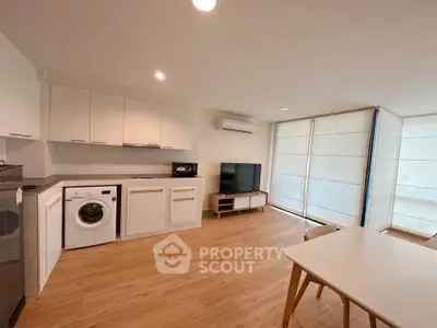 Modern open-plan living room with kitchen, featuring washing machine and stylish furniture.