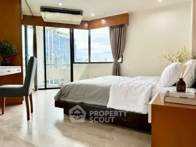 Spacious bedroom with modern decor and city view, featuring large windows and elegant furnishings.