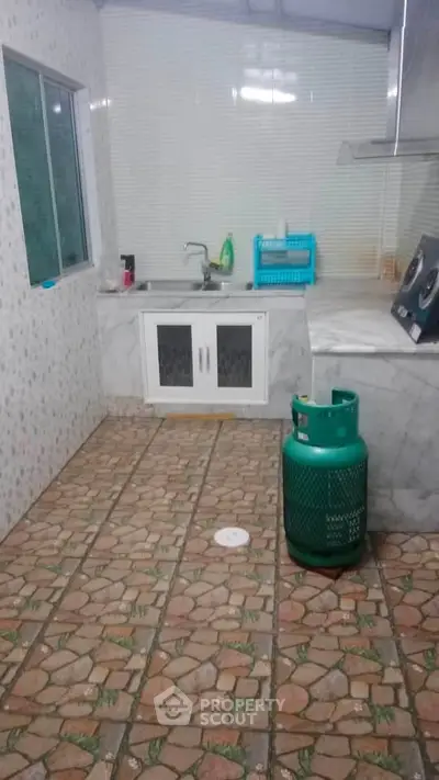Cozy kitchen with tiled floor and gas cylinder, featuring a compact layout and essential appliances.