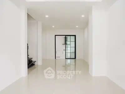 Spacious modern living room with glossy tiled floors and glass door leading to kitchen.