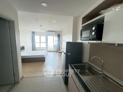 Modern studio apartment with open kitchen and bright bedroom area, featuring sleek appliances and large windows.