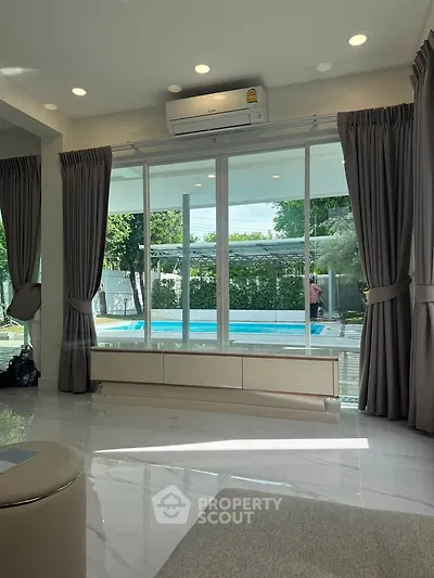 Spacious living room with pool view and large windows, perfect for relaxation.