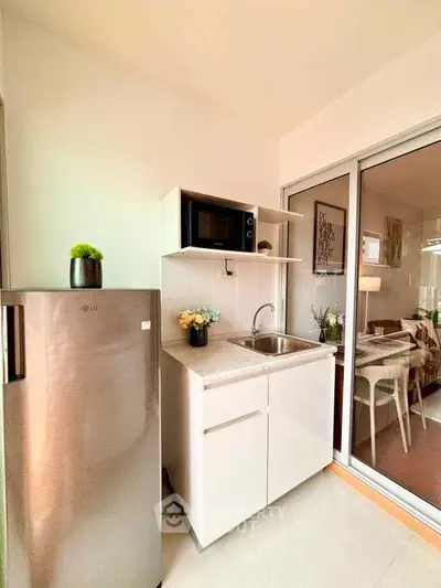 Modern compact kitchen with stainless steel fridge and microwave, adjacent to a cozy dining area.