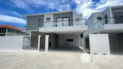 Modern two-story house with sleek balcony and spacious driveway under clear blue sky.