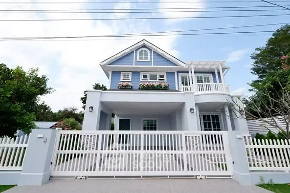 Charming blue two-story house with white picket fence and lush greenery.