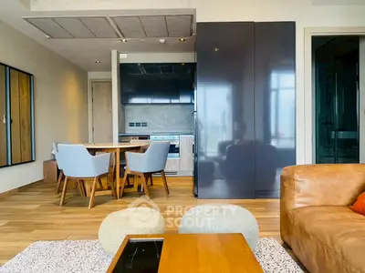 Modern open-plan living room with stylish kitchen and dining area, featuring sleek furniture and wooden flooring.