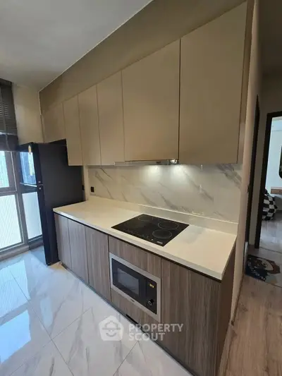 Modern kitchen with sleek cabinetry and built-in appliances, featuring an electric cooktop and microwave.