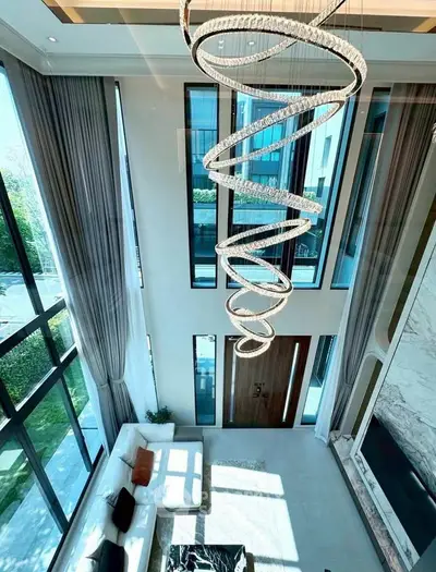 Luxurious living room with high ceilings and modern spiral chandelier, featuring large windows and elegant decor.
