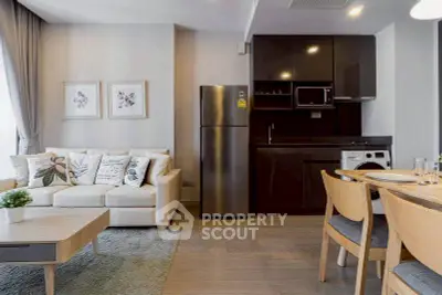Modern living room with sleek kitchen, featuring stainless steel fridge and cozy dining area.