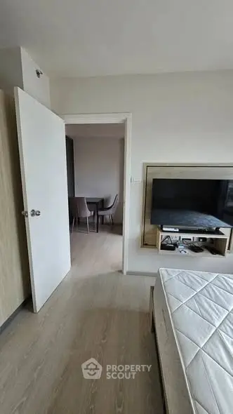Modern bedroom with open door leading to dining area, featuring sleek wooden flooring and minimalist decor.