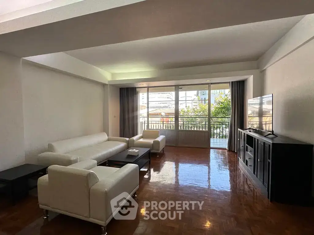 Spacious living room with modern white furniture and large windows offering natural light and city views.