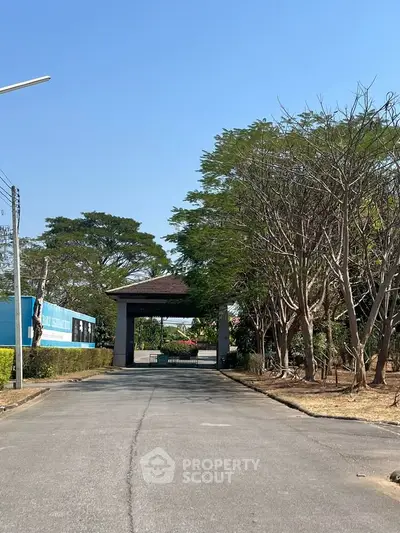 Charming gated entrance with lush greenery and clear blue sky, perfect for serene living.