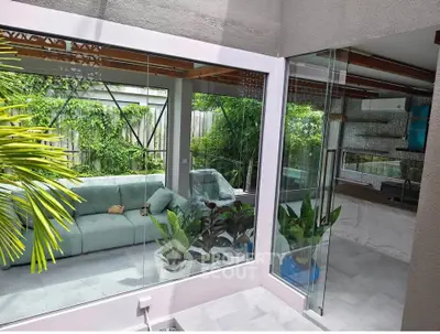Modern indoor-outdoor living space with glass walls and lush greenery