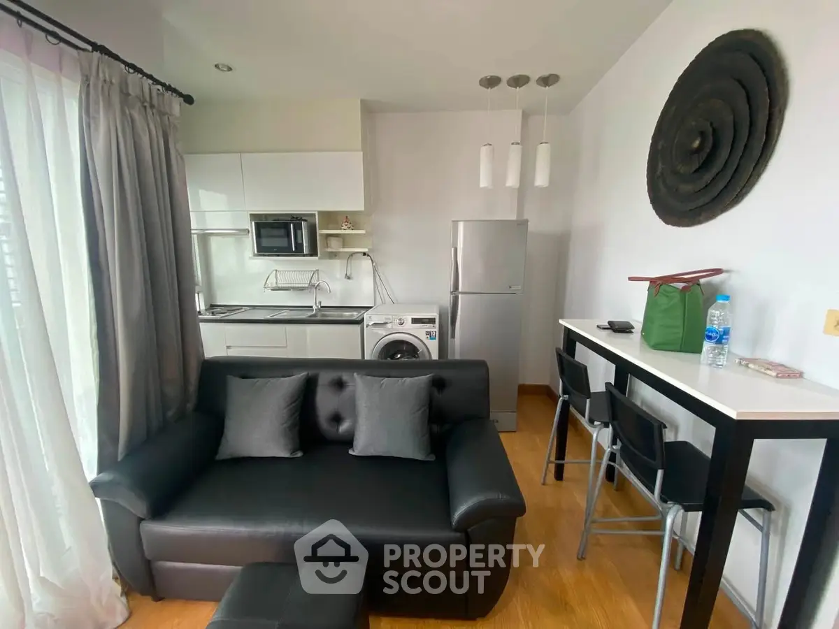 Modern living room with sleek black sofa, compact kitchen, and stylish decor in a cozy apartment.