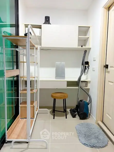 Compact study area with desk, shelves, and vacuum cleaner in modern apartment.