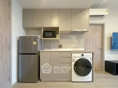Modern kitchen with sleek cabinetry, fridge, microwave, and washing machine in compact layout.